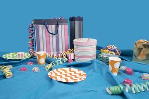 Messy party table with gift bags and boxes, plastic plates and cups on a table with a blue tablecloth against a light blue background photo