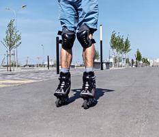 piernas masculinas en patines y equipo de protección de cerca montando en la carretera asfaltada en verano, patinando foto