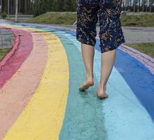 Female legs close up on barefoot on wet asphalt drawn rainbow walking path after rain among puddles photo