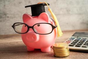 Pigging bank wearing eyeglass with coin, calculator and graduation hat, saving bank education concept. photo