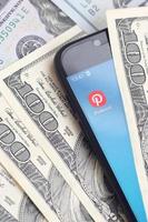 KHARKOV, UKRAINE - MAY 3, 2021 Smartphone screen with Pinterest app and lot of hundred dollar bills. Business and social networking concept photo