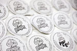 KHARKOV, UKRAINE - MAY 3, 2022 Pringles logo on paper membranes on white wooden table. Pringles is a brand of potato snack chips owned by Kellogg Company photo