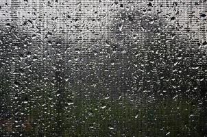Background image of rain drops on a glass window, which is protected by a mosquito net. Macro photo with shallow depth of field