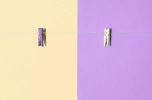 Two colored wooden pegs and small rope lie on texture background of fashion pastel yellow and violet colors photo