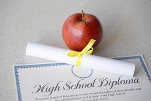 A high school diploma lies on table with small scroll and red apple. Education documents photo