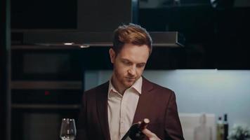 een jong Mens in een pak opent rood wijn gedurende een datum Bij huis. een jong Mens opent een fles van wijn. video