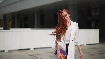 Beautiful confident business woman with red hair in fashion clothes smiles and rejoices. Lady enjoying successful corporate career. Female entrepreneur spinning with happiness downtown. Slow motion. video