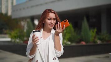 Beautiful business woman smiling and using mobile phone records voice message. Young successful lady next to corporate office talking on phone. Modern Female entrepreneur with smartphone. Slow motion. video