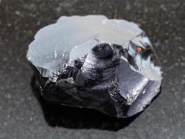 rough obsidian volcanic glass crystal on dark photo