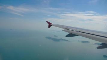 avion survolant la mer bleue et l'île tropicale. aile d'avion à travers le hublot. regardant par la fenêtre des aéronefs pendant le vol video