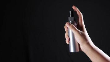 A hand using silver spray bottle on dark background video