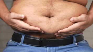 A overweight man touches his belly