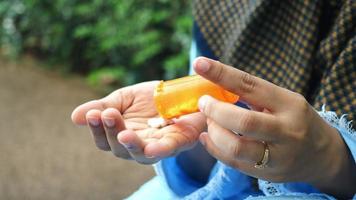 Woman seated outside empties pills into hand from an orange pharmacy bottle video