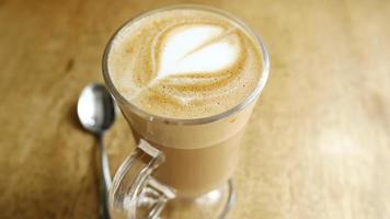 Latte with foam art in a clear glass mug on a table with spoon video