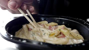 Creamy penne pasta in plastic container eaten with chopsticks video