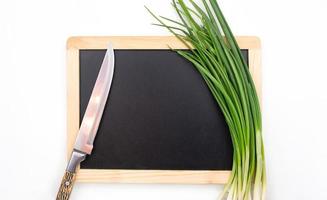 Green onion and knife on cutting black board on isolated background. Ingredient, preparation. Copy space photo