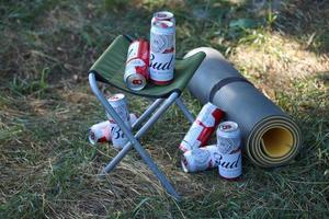SUMY, UKRAINE - AUGUST 01, 2021 Few Cans of Budweiser Lager Alcohol Beer on fisherman chair outdoors. Budweiser is a Brand from Anheuser-Busch Inbev photo