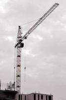 Working tall cranes inside place for with tall buildings under construction against a clear blue sky. Crane and building working progress. Retro tone photo