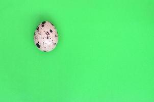 One quail egg on a light green surface, top view, empty place fo photo