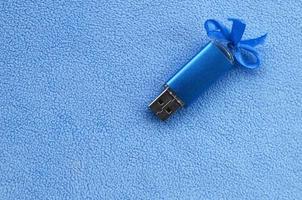 la tarjeta de memoria flash usb azul brillante con un lazo azul se encuentra sobre una manta de tela de vellón azul claro suave y peluda. diseño clásico de regalo femenino para una tarjeta de memoria foto