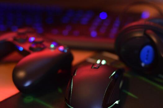 Modern gamepad and gaming mouse lies with keyboard and headphones on table in dark playroom scene. Video game speedrun concept or Esports competition challenge photo