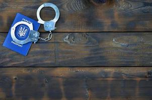 A Ukrainian passport with police handcuffs lies on a wooden table. Problems with the law during the crossing of the borders of countries. The illegal side of visa-free travel for Ukrainian citizens photo