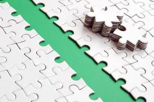 The green path is laid on the platform of a white folded jigsaw puzzle. The missing elements of the puzzle are stacked nearby. Texture image with space for text photo
