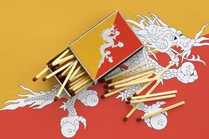 Bhutan flag is shown on an open matchbox, from which several matches fall and lies on a large flag photo