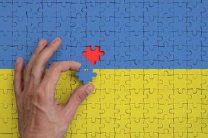 Ukraine flag is depicted on a puzzle, which the man's hand completes to fold photo