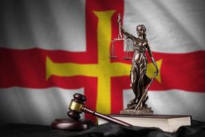 Guernsey flag with statue of lady justice, constitution and judge hammer on black drapery. Concept of judgement and guilt photo