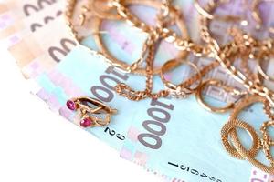 Many expensive golden jewerly rings, earrings and necklaces with big amount of Ukrainian money bills. Pawnshop or jewerly shop concept. Jewelry trading photo