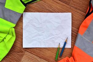 A crumpled sheet of paper with two pencils surrounded by green a photo