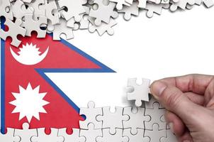 Nepal flag is depicted on a table on which the human hand folds a puzzle of white color photo