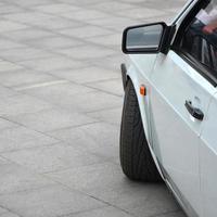 Diagonal view of a white glossy car that stands on a square of gray tiles photo