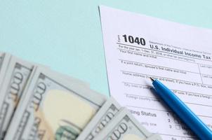 1040 tax form lies near hundred dollar bills and blue pen on a light blue background. US Individual income tax return photo