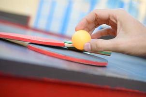 Male hand holds ping pong ball on small tennis table in outdoor sport yard. Active sports and physical training concept photo