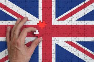 Great britain flag is depicted on a puzzle, which the man's hand completes to fold photo