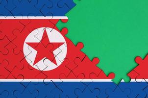 North Korea flag is depicted on a completed jigsaw puzzle with free green copy space on the right side photo