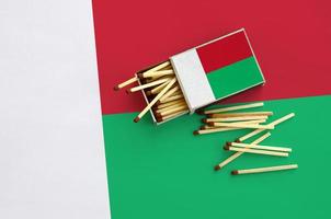 Madagascar flag is shown on an open matchbox, from which several matches fall and lies on a large flag photo