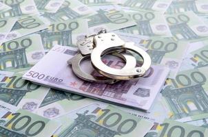 Police handcuffs lies on a set of green monetary denominations of 100 euros. A lot of money forms an infinite heap photo