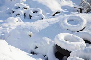 Used and discarded car tires lie on the side of the road, covered with a thick layer of snow photo