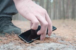 Male hand picking up lost mobile phone from a ground in autumn fir wood path. The concept of finding a valuable thing and good luck photo