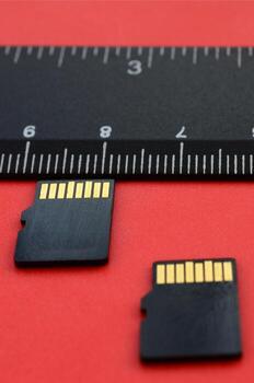 Two small micro SD memory cards lie on a red background next to a black ruler. A small and compact data and information store photo