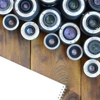 Several photographic lenses and white notebook lie on a brown wooden background. Space for text photo