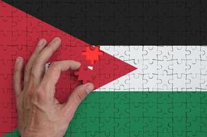 Jordan flag is depicted on a puzzle, which the man's hand completes to fold photo
