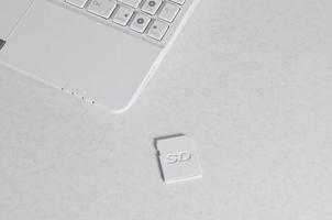 A compact SD memory card lies on a white netbook. The digital information storage device is ready for use. Concept of modern technologies photo