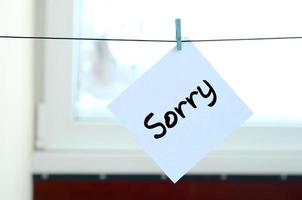 Sorry. Note is written on a white sticker that hangs with a clothespin on a rope on a background of window glass photo