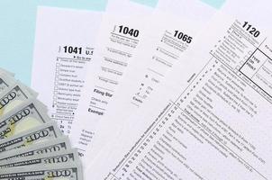 Tax forms lies near hundred dollar bills and blue pen on a light blue background. Income tax return photo