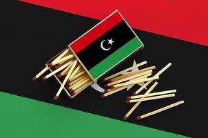 la bandera de libia se muestra en una caja de cerillas abierta, de la que caen varias cerillas y se encuentra en una bandera grande foto
