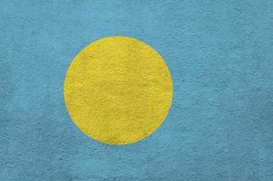 Palau flag depicted in bright paint colors on old relief plastering wall. Textured banner on rough background photo